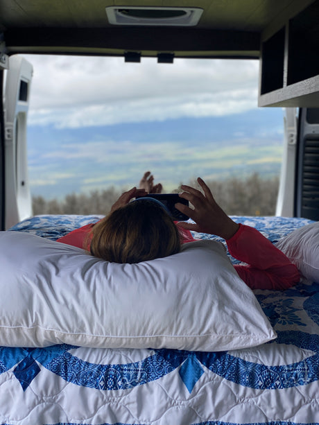 Enjoying comfort in an RV rental, a person relaxes on a bed, phone in hand, admiring the scenic view.