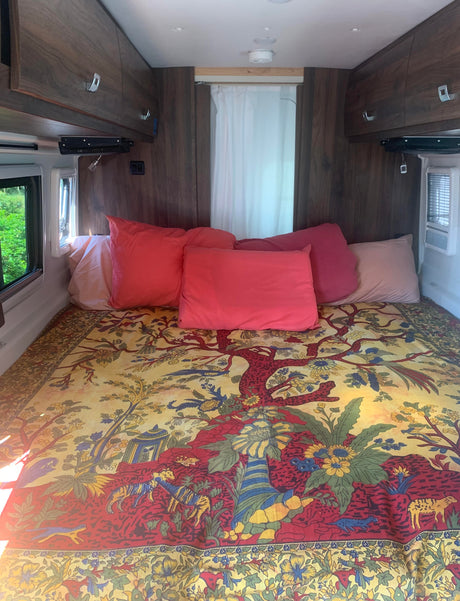Inside an RV rental: a vibrant bed with an ornate tapestry, plush pillows, and built-in wood cabinets.