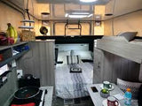 Interior of a modern RV rental: a cozy rear bed, elevated bunk, compact kitchen, and dining area. Perfect for travel!