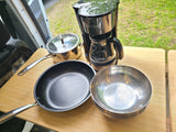 RV rental kitchen setup: coffee maker, pot, pan, and bowls on a wood table, ready for campsite meals.