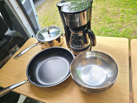 RV rental kitchen setup: coffee maker, pot, pan, and bowls on a wood table, ready for campsite meals.