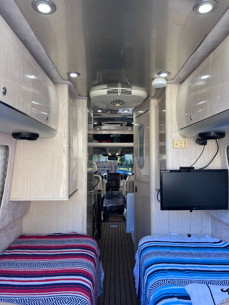 RV rental interior: A bright, modern compact living space with twin beds, overhead cabinets, and a view to the cockpit.