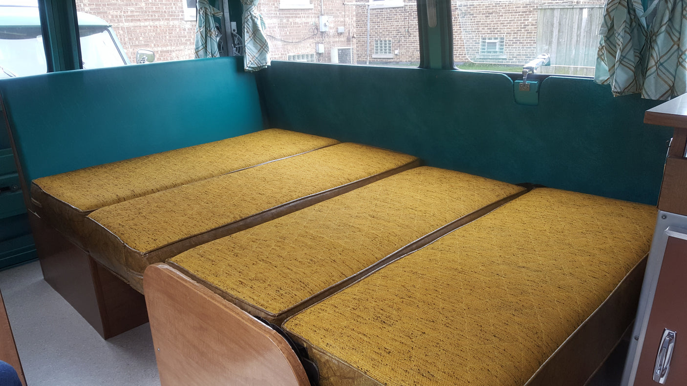 Cozy RV rental interior with a gold-cushioned bed and teal walls, ideal for relaxed travel.