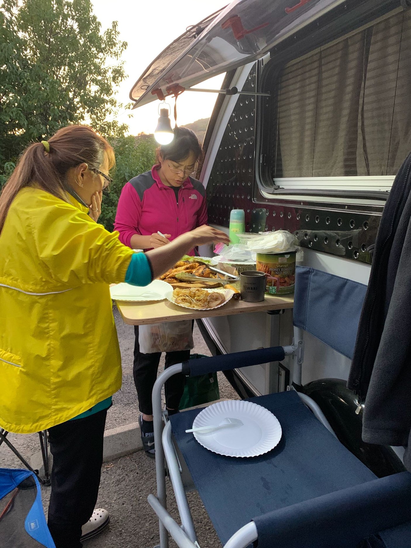 Two women prepare dinner outdoors by their RV rental, serving food from a portable table.