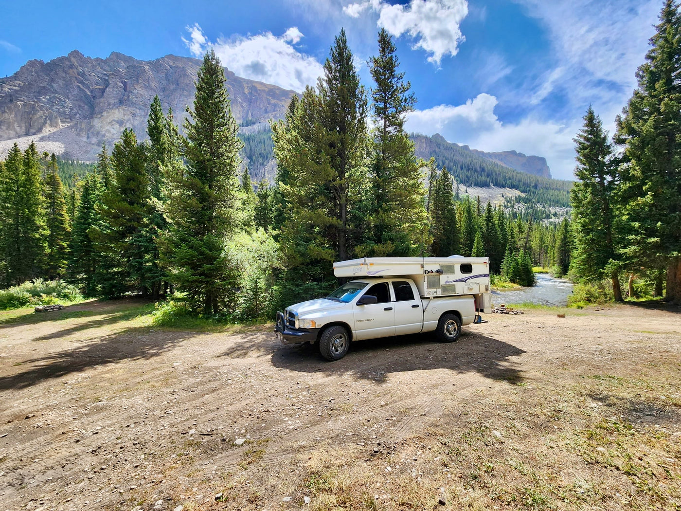 Scenic mountain camping! An RV rental truck camper rests on a dirt clearing by a river — photo 1