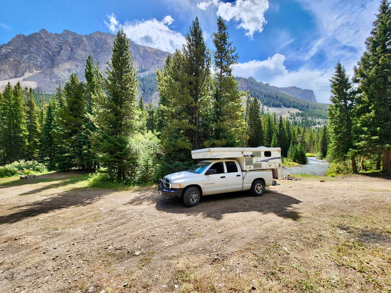 Scenic mountain camping! An RV rental truck camper rests on a dirt clearing by a river — photo 1