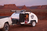 This RV rental teardrop camper, hitched to a truck, awaits desert camping adventures under a twilight sky.