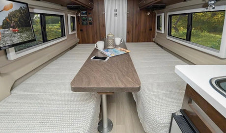 Cozy RV rental interior: two beds with a central dining table and scenic windows, perfect for travel.