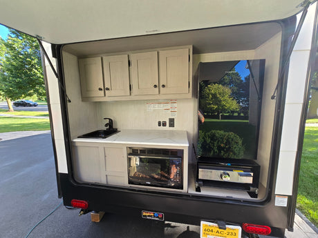 This RV rental shows a compact outdoor kitchen with a sink, microwave, fridge, and grill.