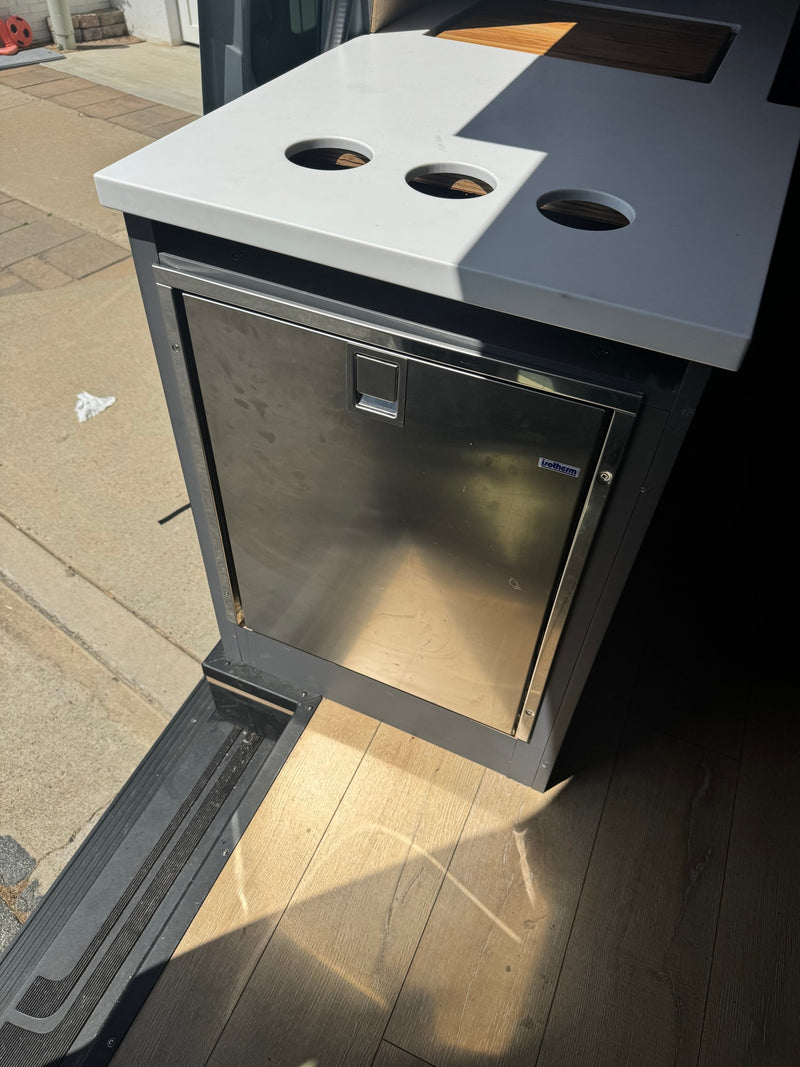 RV rental interior: built-in Isotherm fridge, sleek countertop with three round openings, and light wood flooring. — photo 12