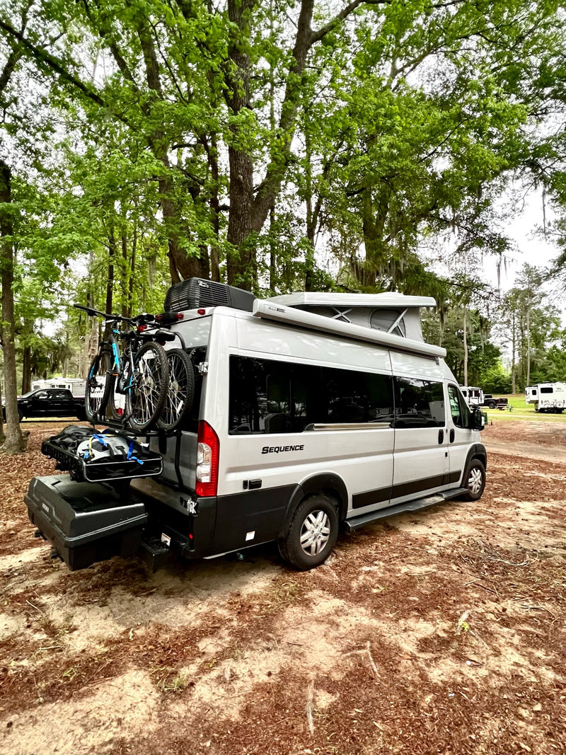  rests on gravel under a grand tree canopy.|Gray pop-top RV rental at a lakeside campground — photo 3