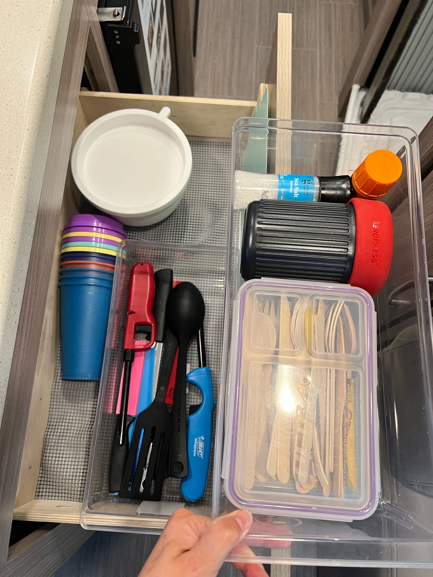 Neatly organized rv rental kitchen drawer with colorful cups, utensils, AeroPress, salt grinder, and wooden cutlery.