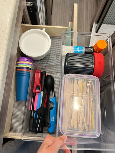 Neatly organized rv rental kitchen drawer with colorful cups, utensils, AeroPress, salt grinder, and wooden cutlery.