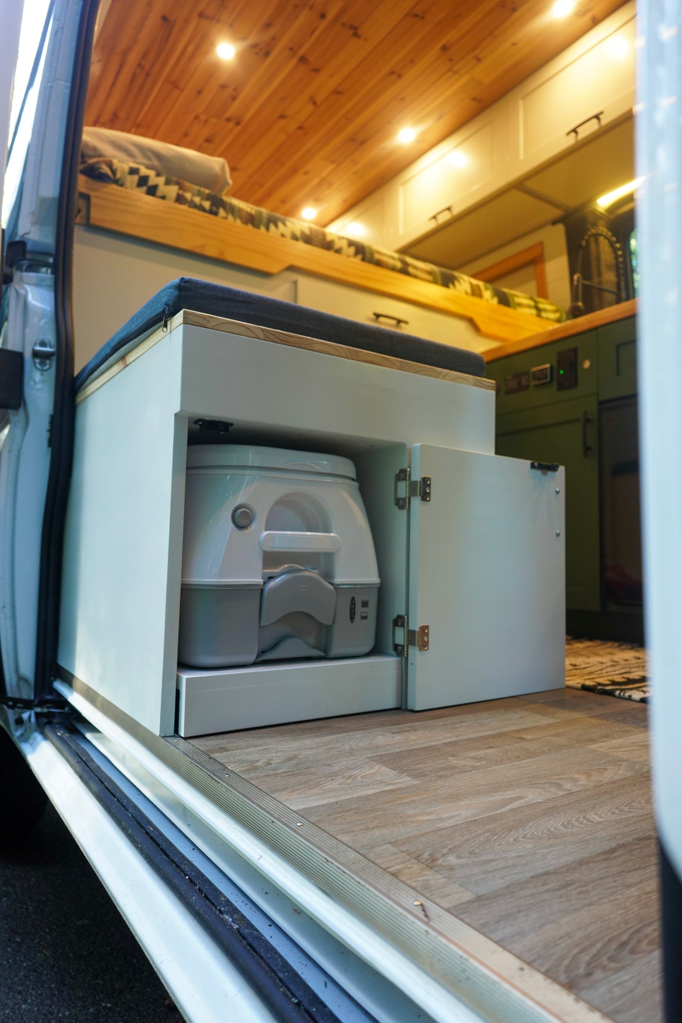RV rental: Campervan interior showing a pull-out portable toilet under a bench seat, with a bed and kitchen area.