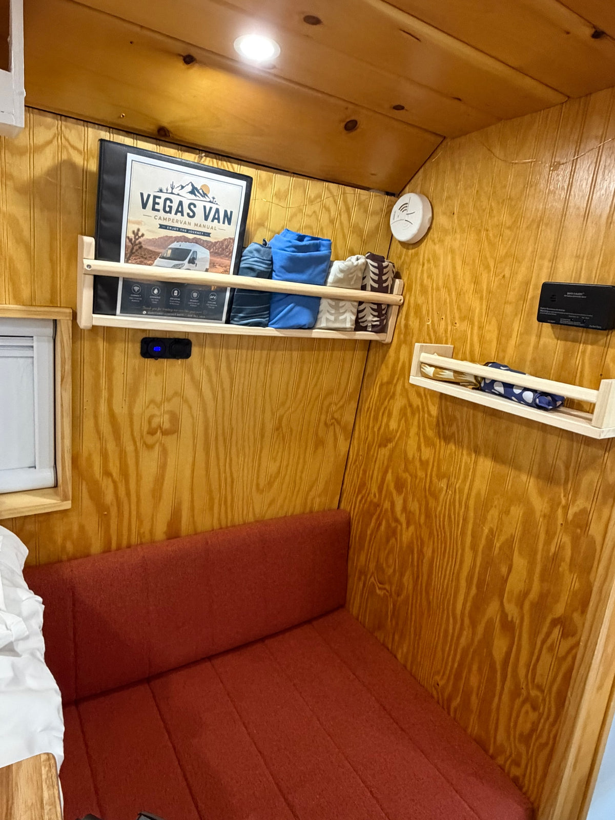 Cozy rv rental interior featuring wooden paneling, a red upholstered bench, and shelves with a "Vegas Van" manual. — photo 14