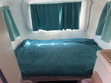 Comfortable sleeping area inside an RV rental, featuring a bed with teal covers and matching curtains. Sunlight illuminates the space.