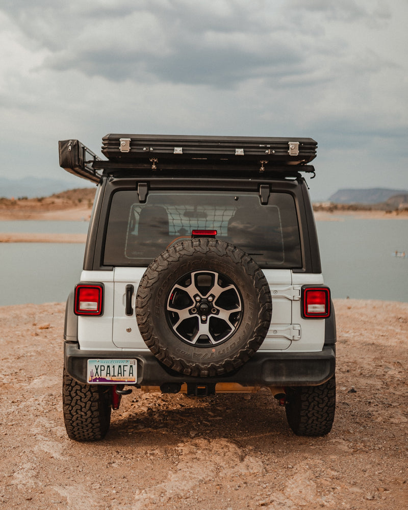 A white Jeep Wrangler with a rooftop tent, ideal for an RV rental adventure, is parked by a scenic lake under cloudy skies. — photo 4