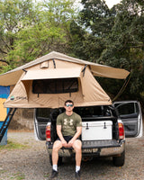 Experience outdoor adventure with this RV rental. Man on truck tailgate by a rooftop tent, perfect for camping trips.