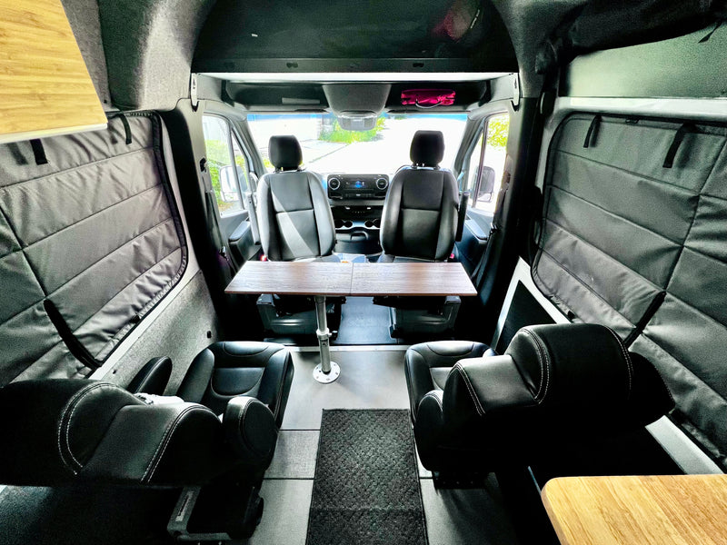 Spacious RV rental interior with swiveling seats, a dining table, and insulated window covers for comfort. — photo 9