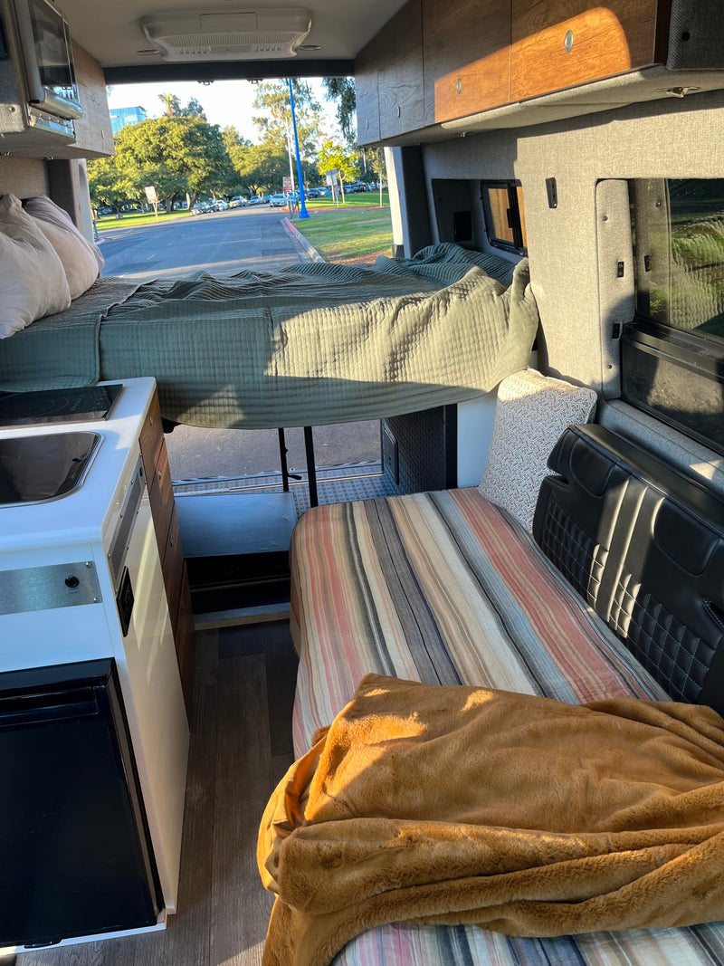 Sunlit RV rental interior featuring a raised bed, compact kitchen, and lower sleeping/seating area. — photo 7