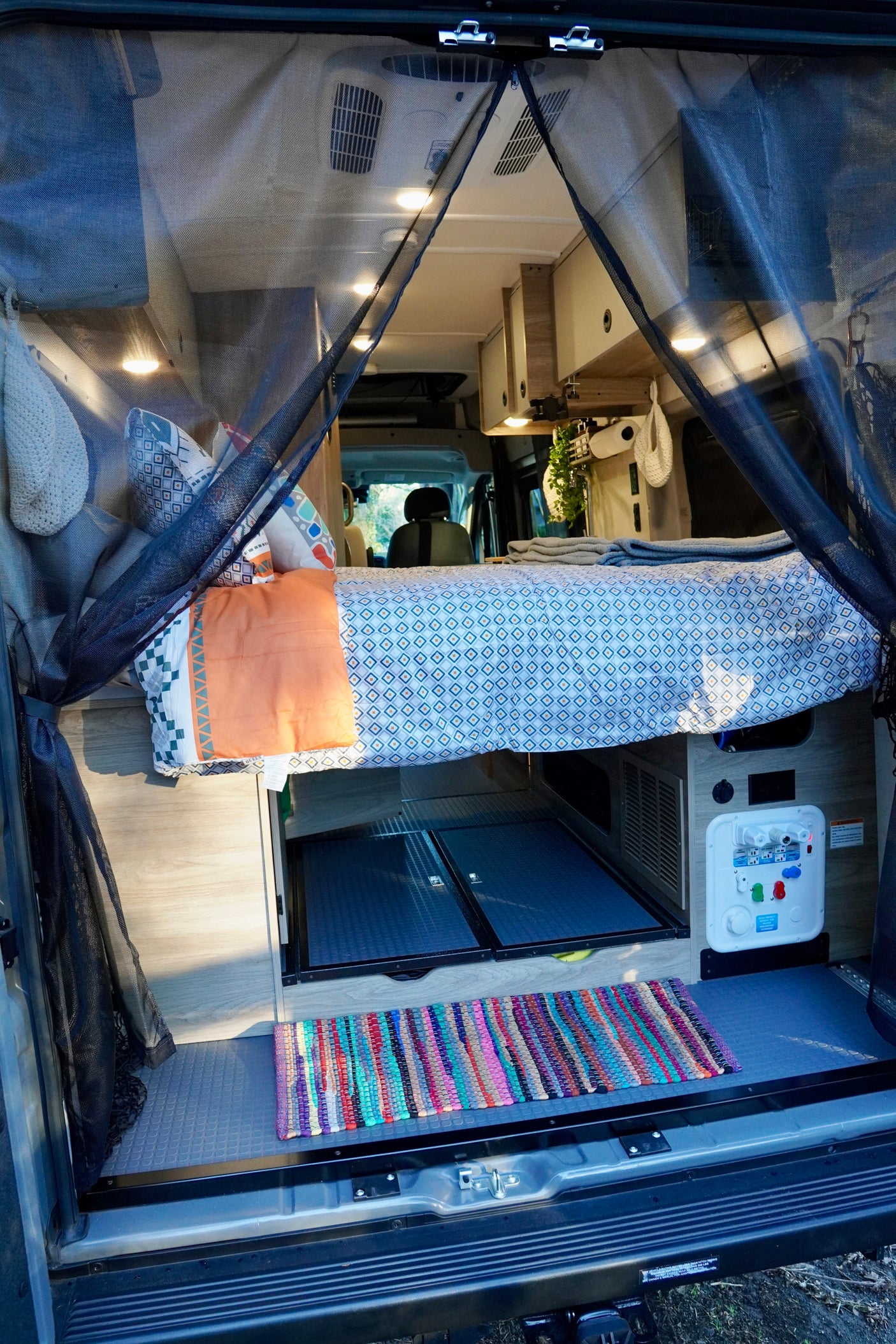 Cozy rv rental interior: view from rear showing bed, storage, and water panel with a mesh screen door. Perfect for travel.