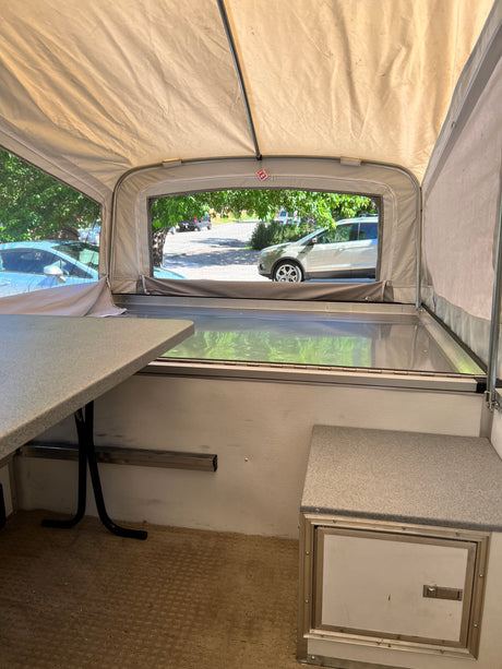 Inside an RV rental: Cozy pop-up camper interior with table, bed, and outdoor views for camping and travel.