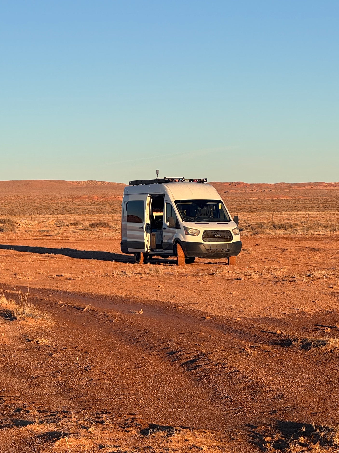 Adventure-ready rv rental van with open door, parked off-road in a wide desert with red earth under a clear sky.