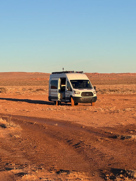 Adventure-ready rv rental van with open door, parked off-road in a wide desert with red earth under a clear sky.