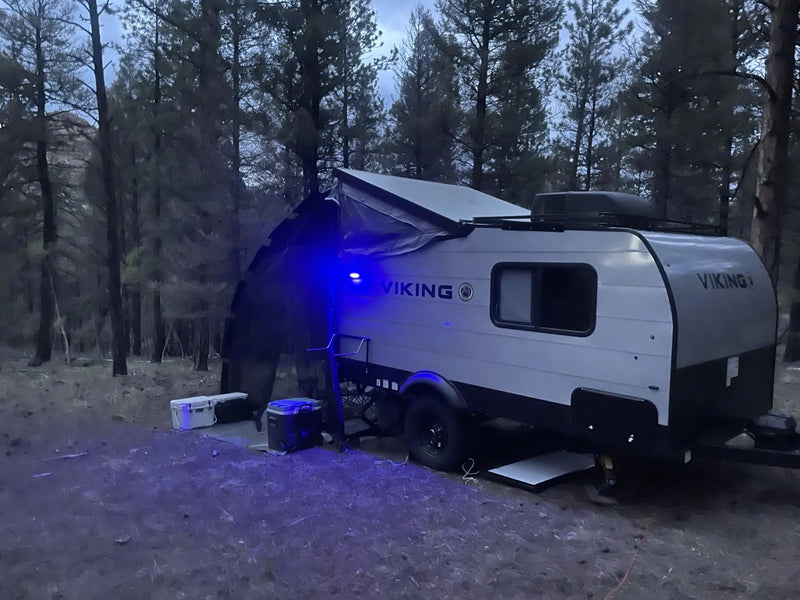 Night camping: A small grey RV rental with an extended awning and blue light — photo 1
