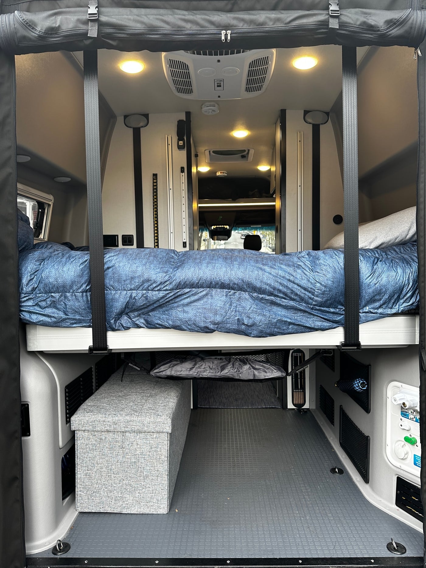 Step inside this RV rental! View of a comfortable bed suspended over storage & utility panels in a spacious camper van interior. — photo 8