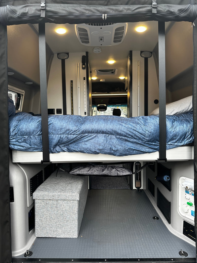 Step inside this RV rental! View of a comfortable bed suspended over storage & utility panels in a spacious camper van interior. — photo 8