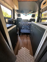 Interior of an RV rental: a spacious camper van with a kitchen, dark cabinets, wood floors, and a Graco baby crib.