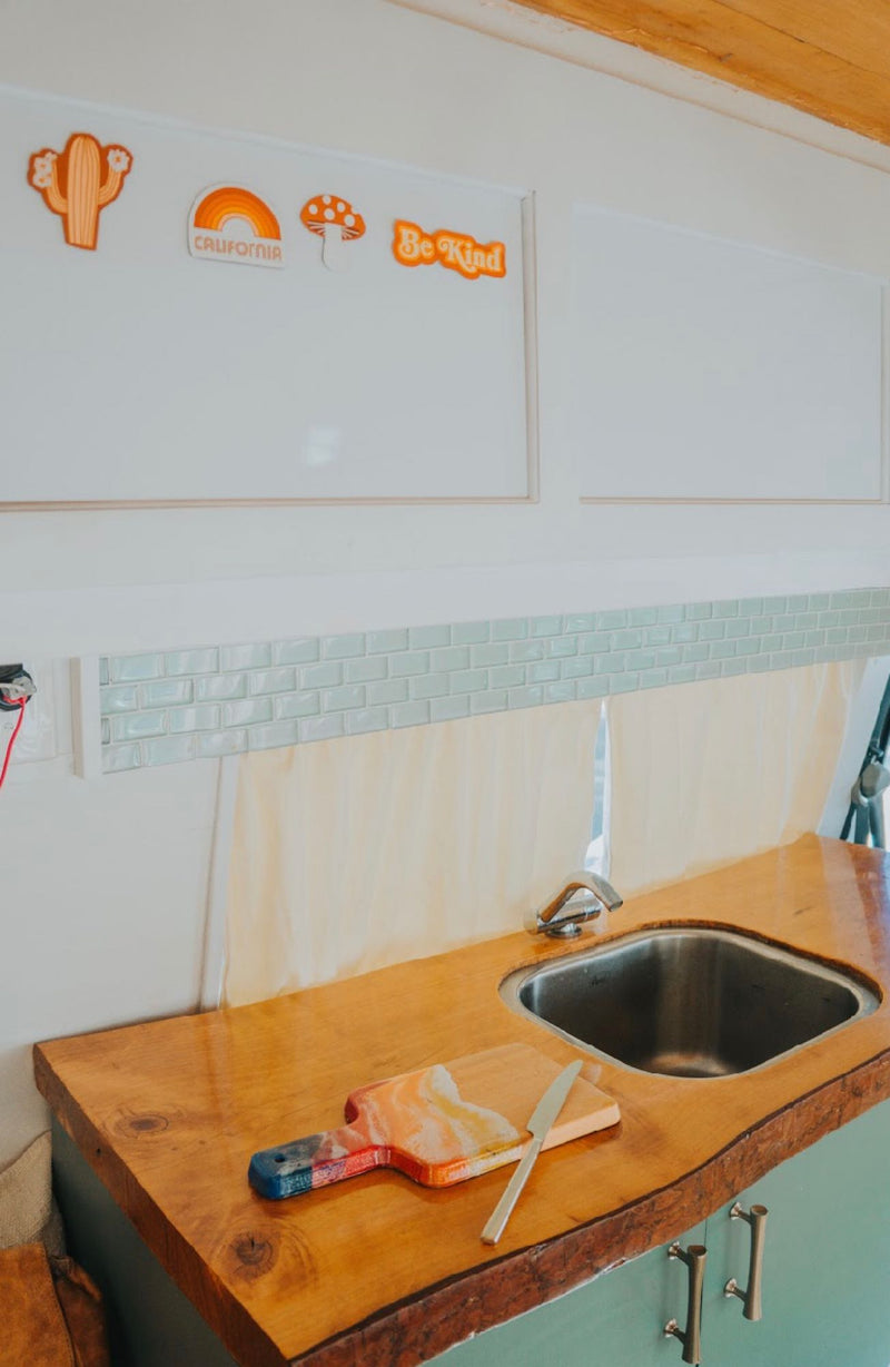Cozy RV rental kitchen featuring a wood counter, stainless steel sink, light blue subway tile backsplash, and fun decals. — photo 17