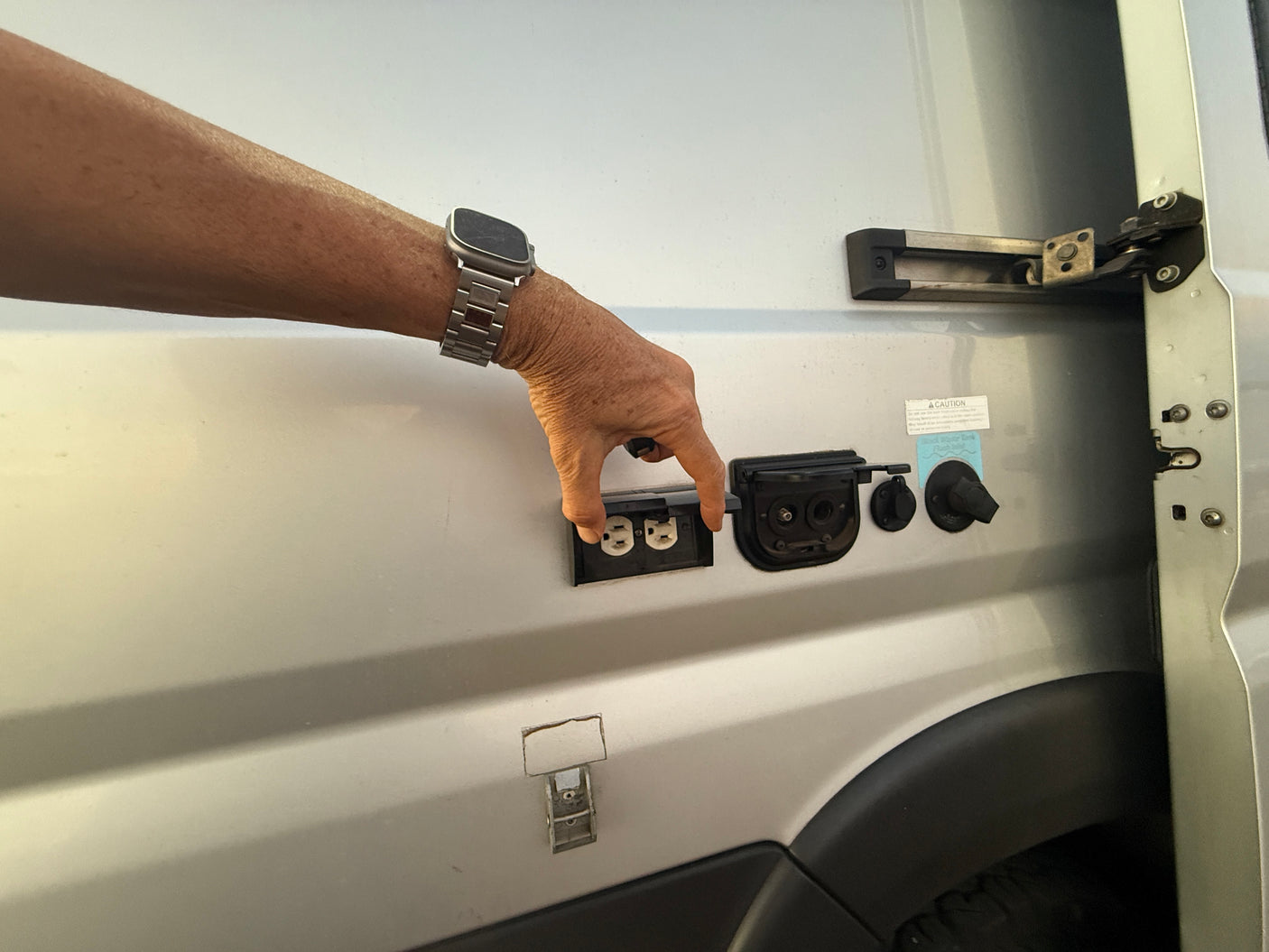 Hand opening external RV rental utility panel showing AC outlets, water hookups.