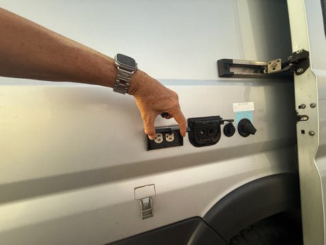 Hand opening external RV rental utility panel showing AC outlets, water hookups.