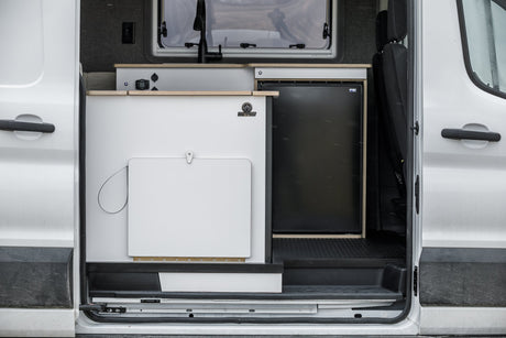 Modern rv rental camper van interior featuring a sleek kitchen counter, sink faucet, and refrigerator.