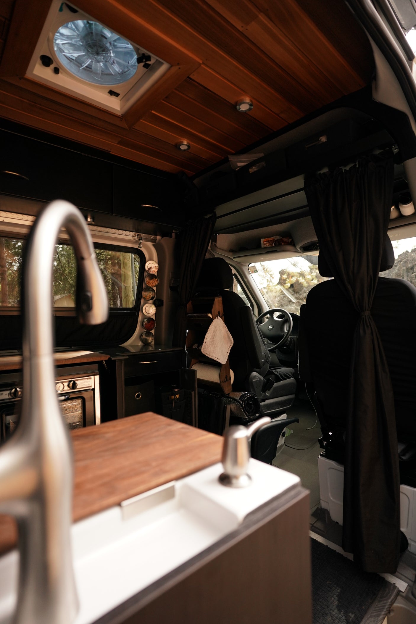 Interior of a modern RV rental, featuring a stylish kitchen with sink and oven, extending to the spacious driver's cab.