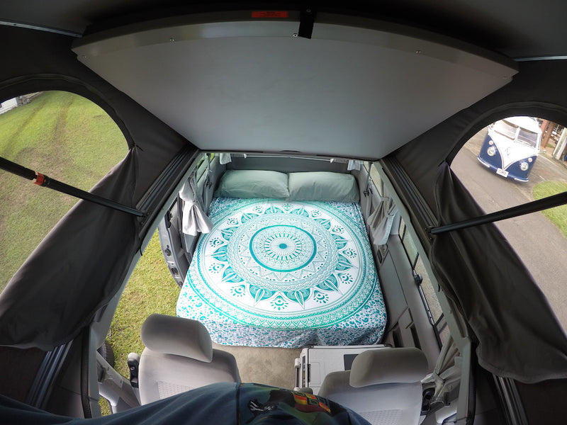 Interior of a pop-top rv rental camper van. Features a bed with a teal mandala design and a view of a vintage VW bus. — photo 11