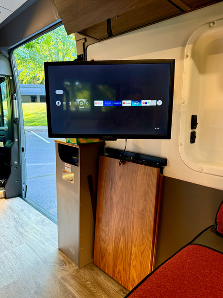 Inside an RV rental: Insignia TV showing streaming apps, foldable table, and open door to nature.