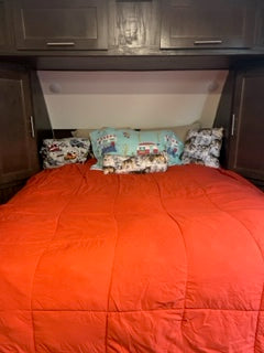 RV rental bedroom: A comfy bed with a red comforter, dark cabinets, and folded bedding in the bunk. Ready for travel adventures!