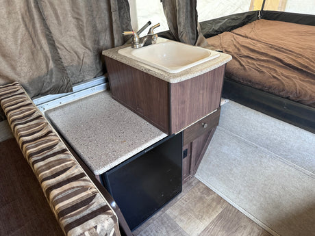 This RV rental interior features a compact kitchenette with a sink, Dometic fridge, and an adjacent sleeping area.