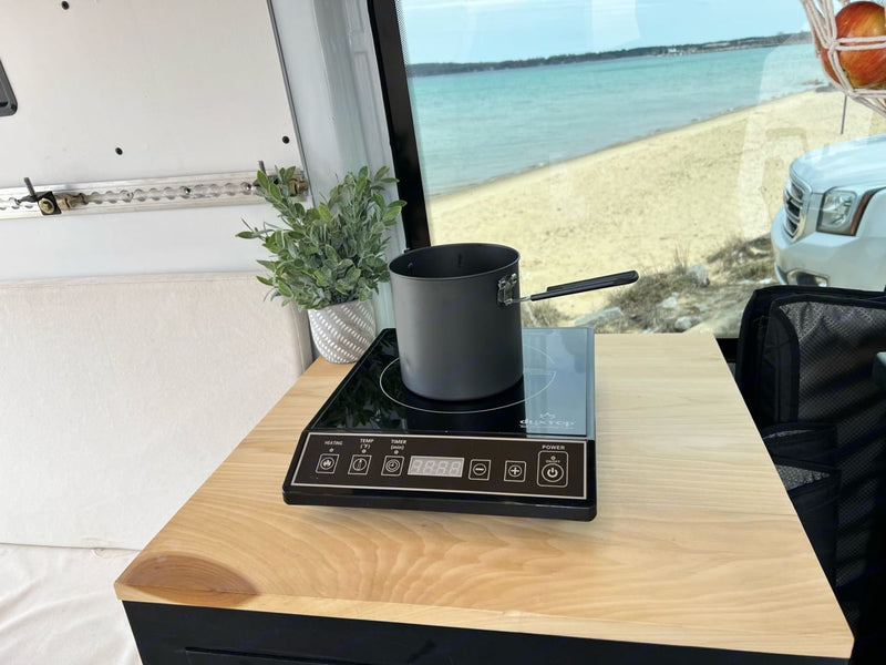  surrounded by bare trees on a gravel lot.|This RV rental offers a sleek van interior with a kitchen — photo 7