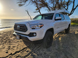 White Toyota Tacoma with rooftop tent RV rental on a Maui beach, perfect for adventure.