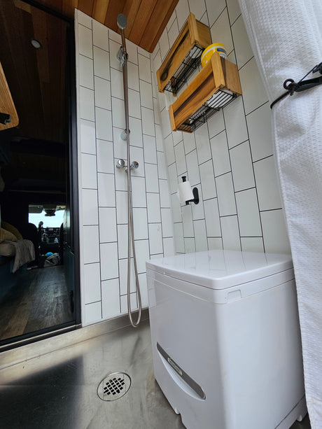 RV rental bathroom with white tiles, wood accents, shower, composting toilet, and compact design. Functional space.