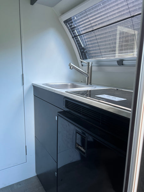 Discover this modern RV rental's compact kitchen, complete with a stainless steel sink, cooktop, and built-in refrigerator.