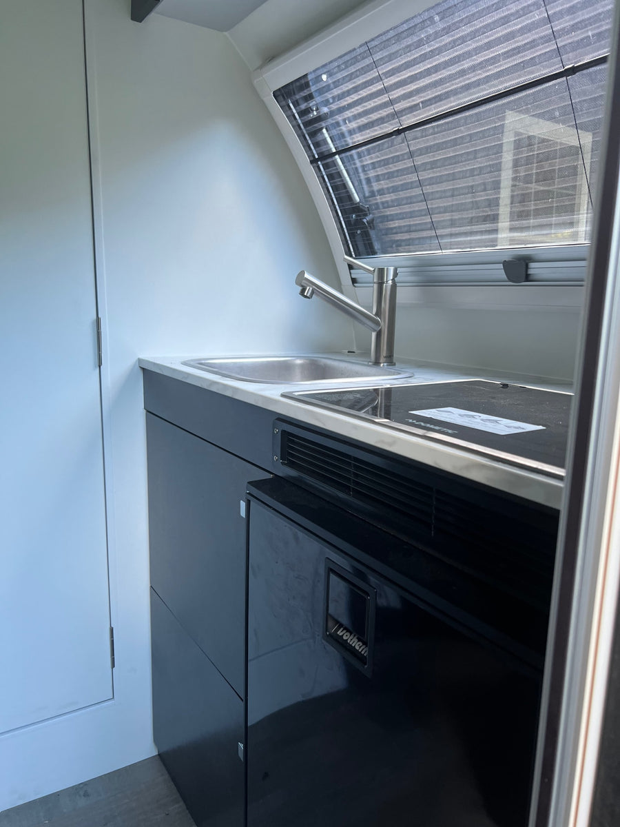 Discover this modern RV rental's compact kitchen, complete with a stainless steel sink, cooktop, and built-in refrigerator.