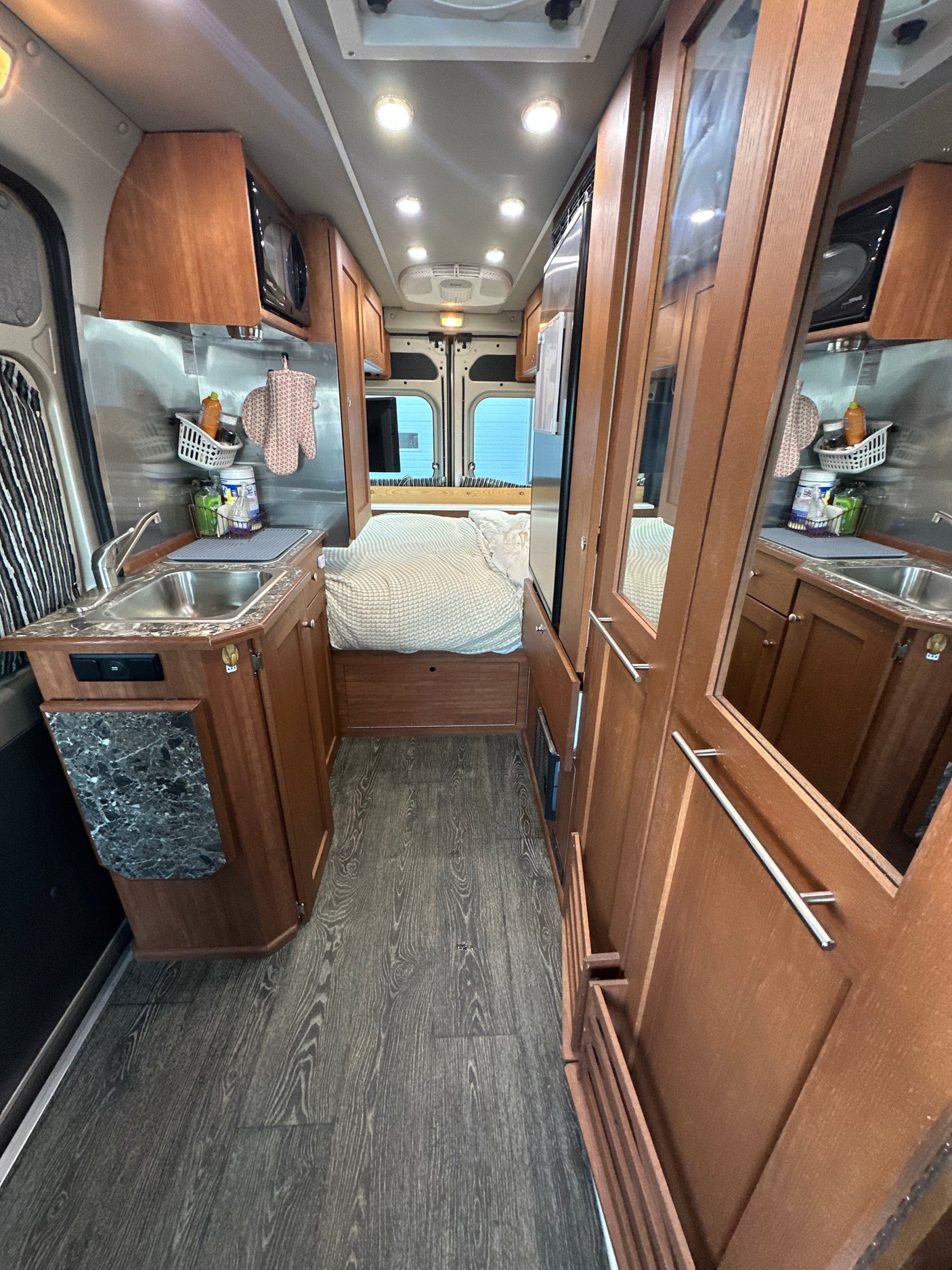 Experience compact living in this RV rental: functional kitchen, cozy bed, and warm wood details.