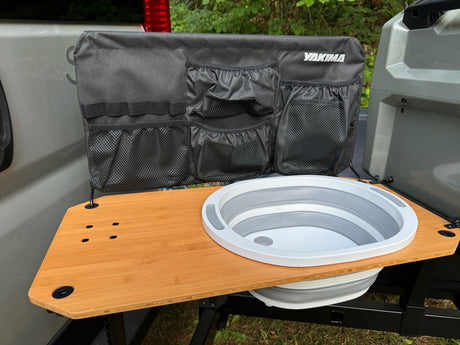RV rental camping setup: A vehicle tailgate with a portable sink, wooden table, and fabric organizer with pockets.