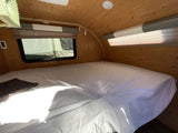 Spacious RV rental bedroom with a comfy bed, wood walls, and windows, perfect for your next adventure.
