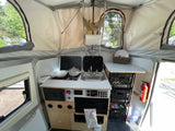 Step into this RV rental's interior: a compact kitchenette, crate storage, and pop-up canvas walls create a cozy space.